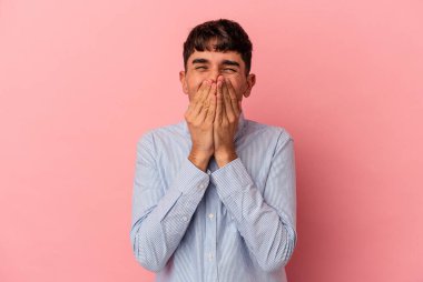 Genç melez adam pembe arka planda izole edilmiş bir şekilde bir şeylere gülüyor, ağızlarını ellerle kapatıyor..