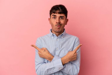 Genç melez adam pembe arka plan noktalarında izole edilmiş, iki seçenek arasında seçim yapmaya çalışıyor..