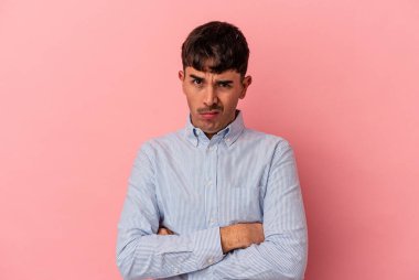 Genç melez adam pembe arka planda izole edilmiş, mutsuz ve alaycı bir ifadeyle kameraya bakıyor..