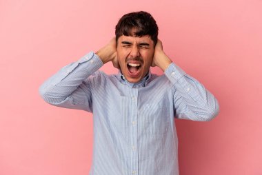 Genç melez adam pembe arka planda izole edilmiş kulakları kulaklarıyla kapatıyor çok fazla ses duymamaya çalışıyor..