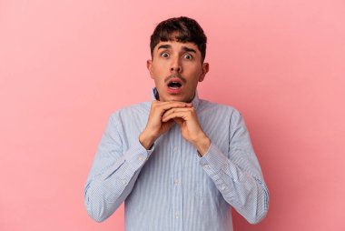 Genç melez adam pembe arka planda izole edilmiş şans için dua ediyor, şaşırmış ve ağzı açık bir şekilde önüne bakıyor..