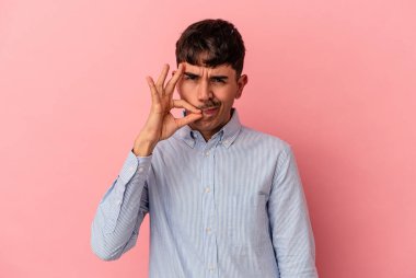 Genç melez adam pembe arka planda izole edilmiş, parmakları dudaklarında bir sır saklıyor..