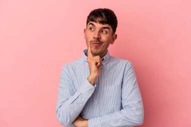 Genç melez adam, pembe arka planda izole edilmiş. Bir strateji planlıyor, bir iş yolu düşünüyor..