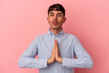 Genç melez adam pembe arka planda izole edilmiş dua ediyor, bağlılık gösteriyor, dindar biri ilahi ilham arıyor..