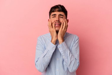 Genç melez adam pembe arka planda izole edilmiş, ağlıyor, bir şeyden memnun değil, acı ve kafa karışıklığı kavramı..
