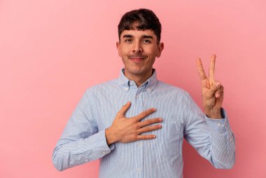 Genç melez adam pembe arka planda izole edilmiş yemin ediyor, elini göğsüne koyuyor..