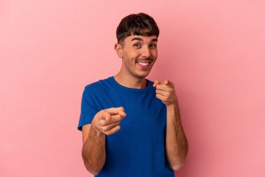 Genç melez adam pembe arka planda izole edilmiş, parmaklarıyla ön tarafı işaret ediyor..
