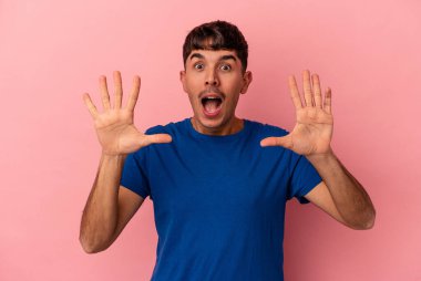 Genç melez adam pembe arka planda izole edilmiş. Hoş bir sürprizle karşılaşıyor, heyecanlı ve el kaldırıyor..