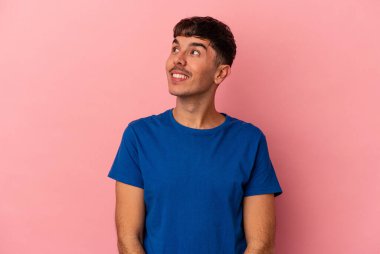Genç melez bir adam pembe arka planda izole edilmiş rahat ve mutlu bir şekilde gülüyor, boynunda dişlerini gösteriyor..