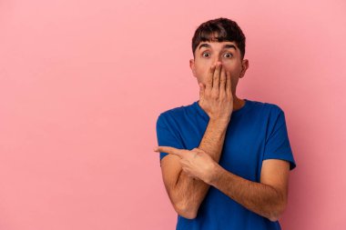 Genç melez adam, pembe arka planda izole edilmiş, kenarı işaret ediyor.