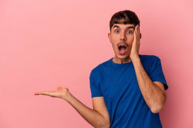 Pembe arka planda izole edilmiş genç melez adam, avuç içinde kopya alanı tutmaktan etkilenmiş..