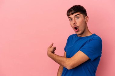Genç melez adam pembe arka planda izole edilmiş gülümseyen ve işaret eden boş alanda bir şey gösteriyor..