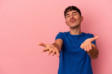 Genç melez adam pembe arka planda izole edilmiş dudaklar kıvrılıyor ve hava öpücüğü göndermek için avuç içi tutuyor..