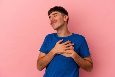 Pembe arka planda izole edilmiş genç melez adam, avuçlarını göğsüne bastıran dostane bir ifadeye sahiptir. Aşk konsepti.