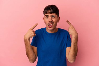 Genç melez adam pembe arka planda izole edilmiş işaret parmağıyla hayal kırıklığı jesti gösteriyor..
