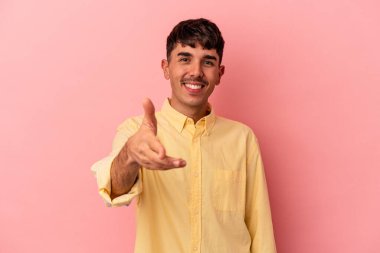 Genç melez adam pembe arka planda izole edilmiş kameraya elini uzatarak selam veriyor..