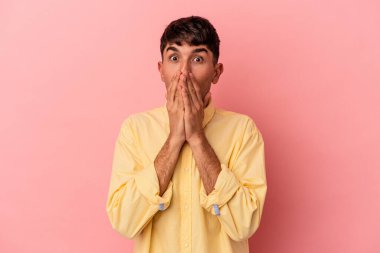 Pembe arka planda izole edilmiş genç melez adam elleriyle ağzını kapatırken şok oldu..