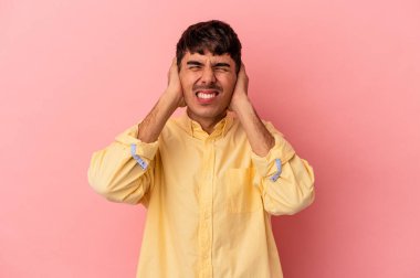 Genç melez adam pembe arka planda izole edilmiş kulakları elleriyle kapatıyor..