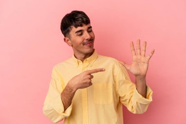 Genç melez adam pembe arka planda izole edilmiş gülümseyen beş numarayı parmaklarıyla gösteriyor..