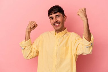 Genç melez adam pembe arka planda izole edilmiş tasasız ve heyecanlı bir şekilde tezahürat yapıyor. Zafer konsepti.