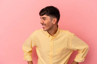 Pembe arka planda yaşayan genç melez adam mutlu bir şekilde gülüyor ve ellerini karnının üstünde tutarak eğleniyor..