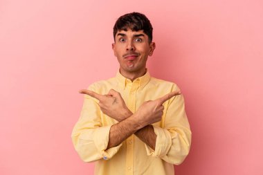 Genç melez adam pembe arka plan noktalarında izole edilmiş, iki seçenek arasında seçim yapmaya çalışıyor..