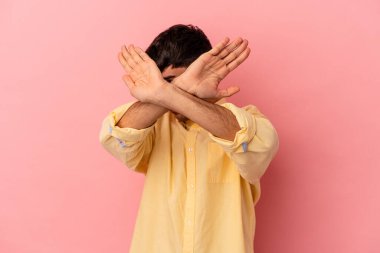 Genç melez adam pembe arka planda izole edilmiş iki kolu çapraz tutuyor, inkar kavramı..