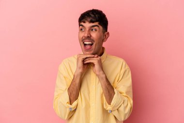 Pembe arka planda izole genç melez adam ellerini çenesinin altında tutuyor, mutlu bir şekilde yana bakıyor..