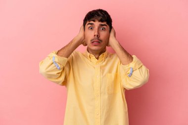 Genç melez adam pembe arka planda izole edilmiş kulakları kulaklarıyla kapatıyor çok fazla ses duymamaya çalışıyor..