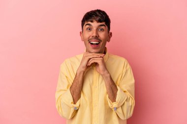 Genç melez adam pembe arka planda izole edilmiş şans için dua ediyor, şaşırmış ve ağzı açık bir şekilde önüne bakıyor..