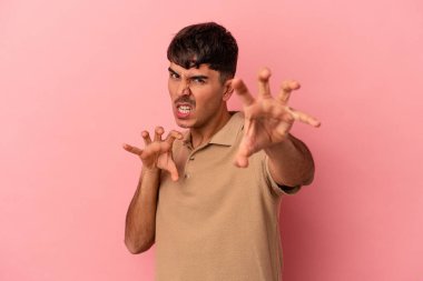 Pembe arka planda izole edilmiş genç melez bir adam pençelerini kedi taklidi yaparken gösteriyor, agresif bir hareket..
