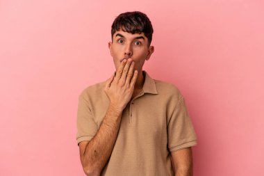 Genç melez adam pembe arka planda izole edilmiş şok olmuş, ağzı ellerle kaplanmış, yeni bir şey keşfetmeye hevesli..