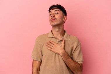 Genç melez adam pembe arka planda izole edilmiş yemin ediyor, elini göğsüne koyuyor..