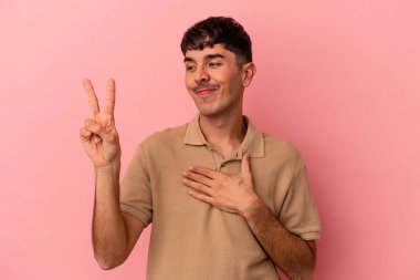 Genç melez adam pembe arka planda izole edilmiş yemin ediyor, elini göğsüne koyuyor..