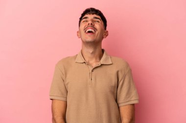 Genç melez bir adam pembe arka planda izole edilmiş rahat ve mutlu bir şekilde gülüyor, boynunda dişlerini gösteriyor..