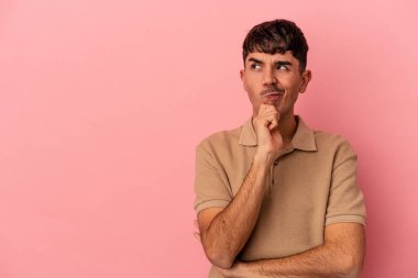 Genç melez adam pembe arka planda izole edilmiş şüpheli ve şüpheci bir ifadeyle yana bakıyor..
