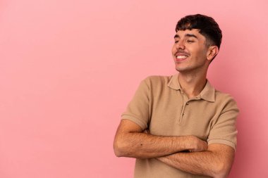 Pembe arka planda soyutlanmış genç melez adam kollarını kavuşturarak gülümsüyor..