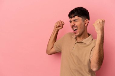 Genç melez adam pembe arka planda izole edilmiş zafer sonrası yumruğunu kaldırıyor, kazanan konsept..