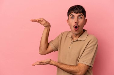 Genç melez adam pembe arka planda izole edilmiş şok olmuş ve hayret içinde elleri arasında bir kopya alanı tutuyor..