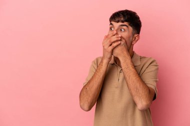 Genç melez adam pembe arka planda izole edilmiş. Düşünceli bir şekilde bir fotokopi odasına bakıyor. Ağzını eliyle kapatıyor..