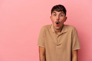 Genç melez adam pembe arka planda izole edilmiş. Gördüğü bir şey yüzünden şoka uğruyor..