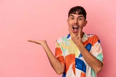 Pembe arka planda izole edilmiş melez genç bir adam avuç içinde fotokopi alanı tutuyor, el üstünde tutuyor. Şaşırmış ve mutlu..