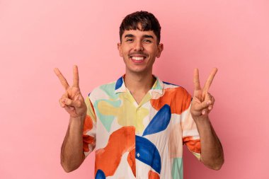 Genç melez adam pembe arka planda izole edilmiş zafer işareti gösteriyor ve gülümsüyor..