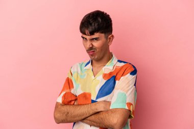 Genç melez adam pembe arka planda izole edilmiş hoşnutsuzca kaşlarını çatmış, kollarını kavuşturmuş..
