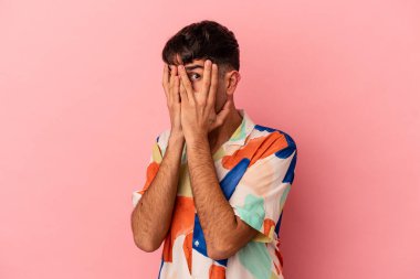 Genç melez adam pembe arka planda izole edilmiş parmaklarıyla gözünü kırp korkmuş ve gergin..