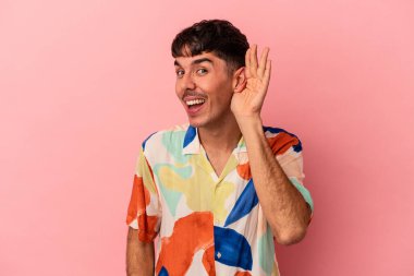 Genç melez adam pembe arka planda izole edilmiş bir şekilde bir dedikoduyu dinlemeye çalışıyor..