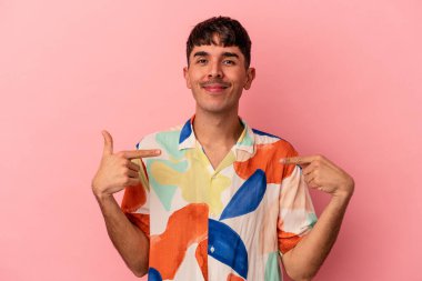 Genç melez adam pembe arka planda izole edilmiş. Elle bir tişört fotokopi alanını işaret ediyor. Gururlu ve kendinden emin.