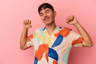 Genç melez adam pembe arka planda izole edilmiş, kollarını uzatmış, rahat bir konumda..