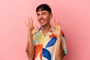 Genç melez adam pembe arka planda izole edilmiş neşeli ve kendine güvenen iyi bir jest yapıyor..