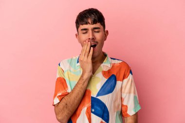 Genç melez adam pembe arka planda izole edilmiş esniyor. Ağzı eliyle kapatan yorgun bir hareket sergiliyor..